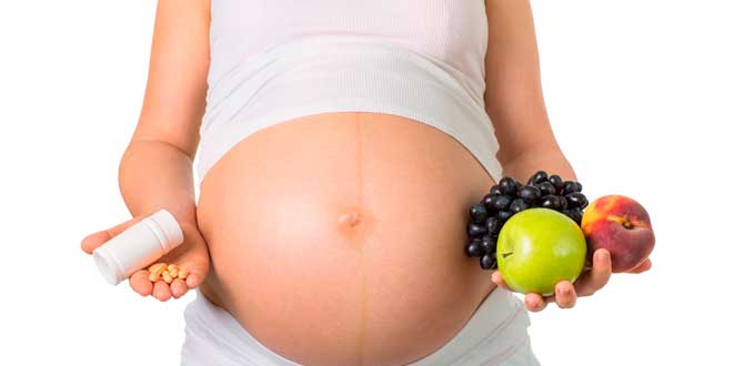 Pregnant woman holding supplements and fruits