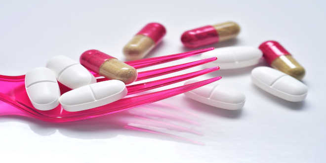 A pink fork with tablets and capsules